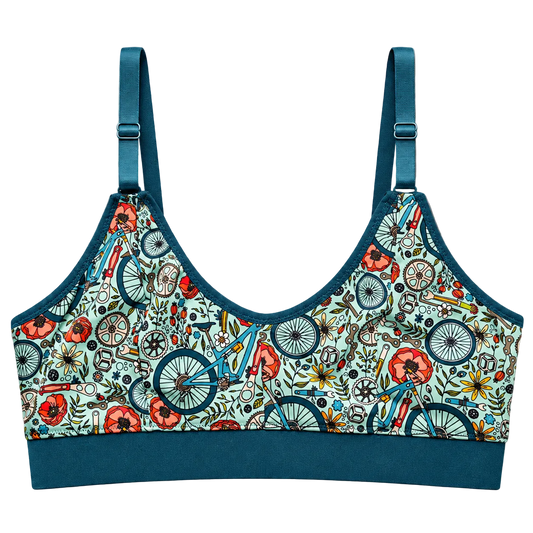SWOOP wireless bra with a teal blue trim and straps, featuring a light blue-green background covered in a detailed bicycle and floral pattern in red, orange, blue, and green.