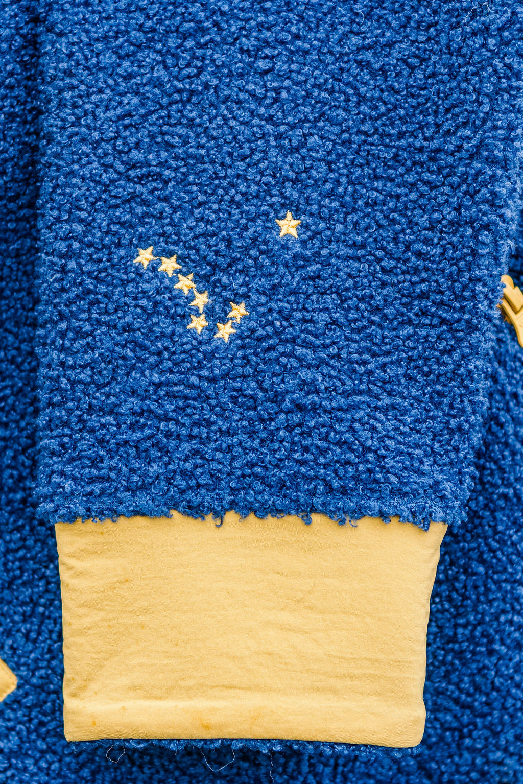 Close-up of a textured royal blue fleece or sherpa fabric with a yellow stitched constellation design and a yellow trim at the bottom.