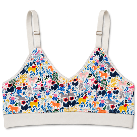 SWOOP wireless bra with adjustable shoulder straps and a white band, featuring a vibrant multicolor unicorn and floral print on a white base, shown against a plain white background.