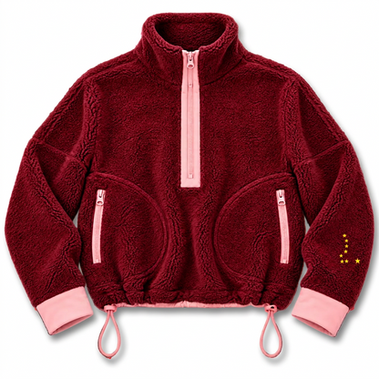 A plush fleece quarter-zip jacket in deep burgundy with light pink trim, cuffs, and hem, featuring zippered pockets and a small yellow embroidered star detail on the sleeve.