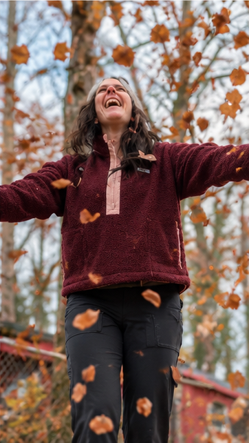 Laughing woman with arms out under falling autumn leaves in the SWOOP Wine Sherpa Fleece Quarter-Zip Pullover